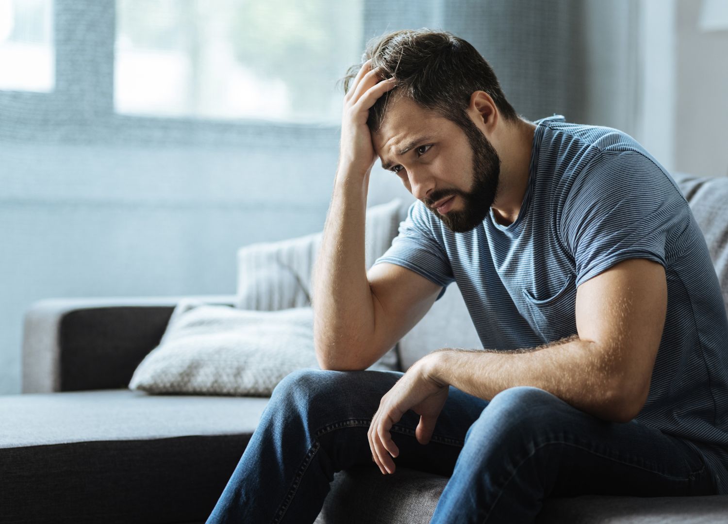 A man sitting on a sofa with his hand resting on his forehead.